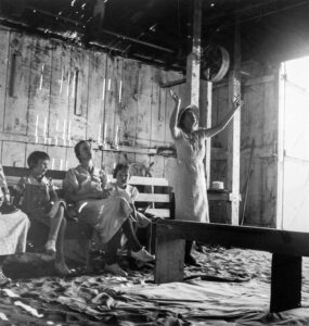 Dorothea Lange (1895 - 1965). "Victory through Christ" Society holding its Sunday Morning Revival in a garage. Dos Palos, California. Testimony: "He's such a wonderful savior, Glory to God. I'm so glad I came to home. Praise God. His love is so wonderful. He's coming soon. I want to praise the Lord for what he is to me. He saved me one time and filled me with the Holy Ghost. Hallalulah! He will fill your heart today with overflowing. Bless His Holy name". Dos Palos, California. June 1938.