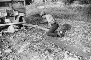 Marion Post Wolcott (1910 - 1990). A mountainer and his wife changing a tire, using a fence post as a jack, on the South Fork of the Kentucky River, Kentucky. August 1940.