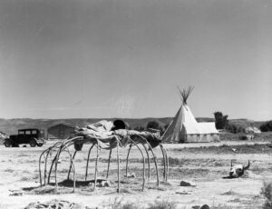 Marion Post Wolcott (1910 - 1990). Steam bath on the Cheyenne Indian Tongue river reservation. A hot fire is made in the center, bricks are heated and water is poured over them. After the Indian gets inside, he is covered with many blankets, and the outside is also covered with cloths and blankets. He stays in there for several hours, sweats and becomes very weak. The skull, outside, is their "medicine". Other Indians watch, stand around and smoke. Lame Deer, Montana. August 1941.