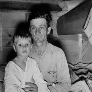 Dorothea Lange (1895 - 1965). This man brought his family, including this sick boy, from Texas in a home-made trailer, five months ago. The father now has work in a potato field. The photograph was made after supper. Merrill, Klamath County, Oregon. October 1939.